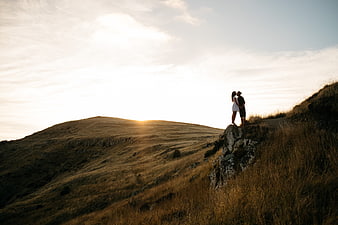 Couple kissing on rocky hilltop at sunset