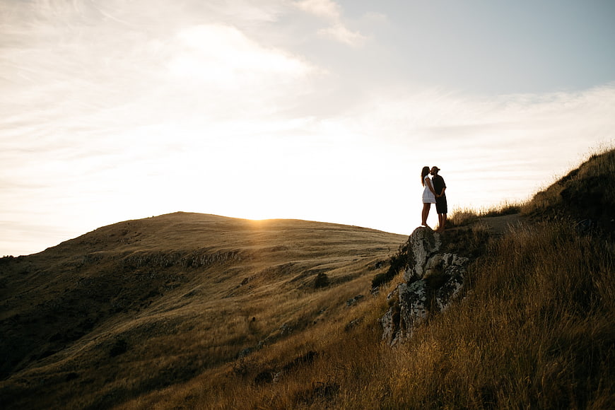 Couple kissing on rocky hilltop at sunset