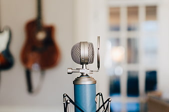 Blue condenser microphone in recording studio with blurred guitars