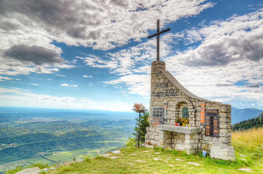 Stone memorial cross on mountain peak with scenic valley view