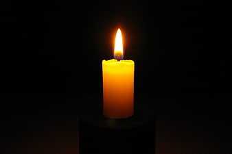 Single lit yellow candle on black background