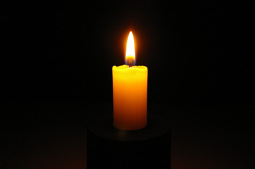 Single lit yellow candle on black background