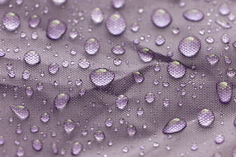Macro shot of water droplets on purple textured fabric