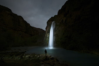 Silhouette of Man Standing Before Glowing Waterfall at Night
