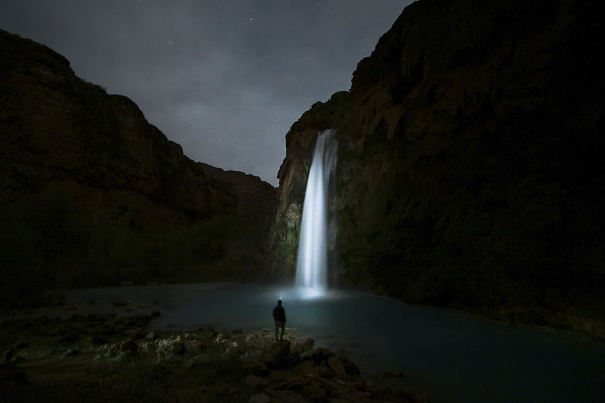 Silhouette of Man Standing Before Glowing Waterfall at Night