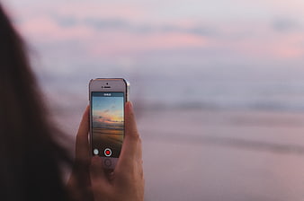 Woman recording sunset video on smartphone at beach