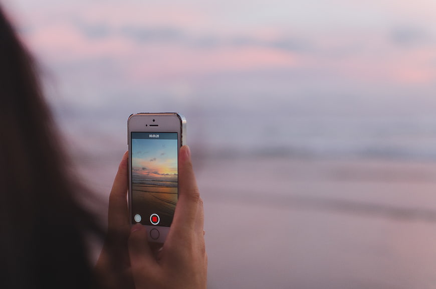 Woman recording sunset video on smartphone at beach