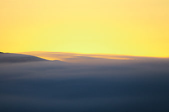 Golden sunset sky above a sea of blue fog and mountains
