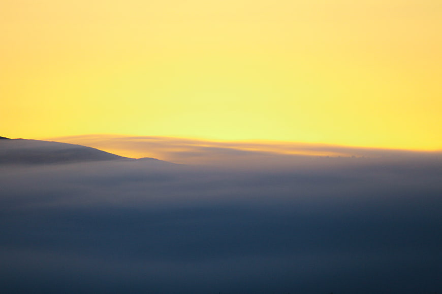 Golden sunset sky above a sea of blue fog and mountains