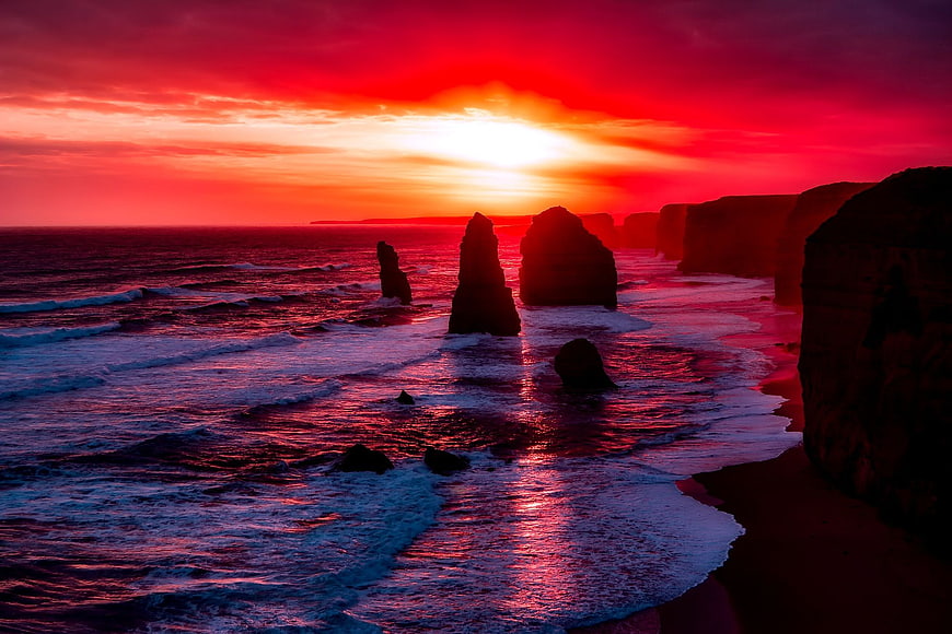 Dramatic red sunset over ocean rock formations and cliffs