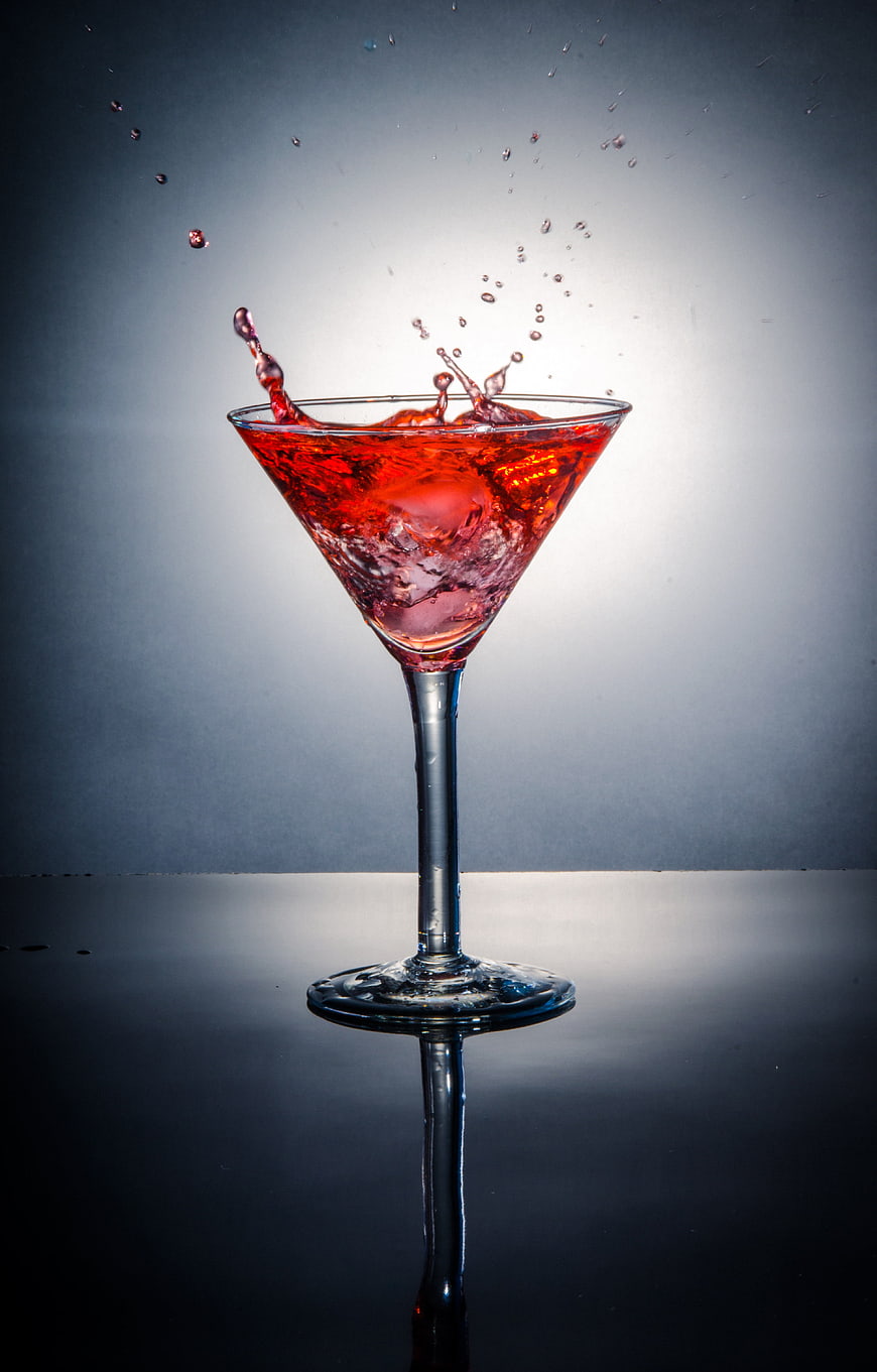 Red cocktail splash in martini glass on dark background