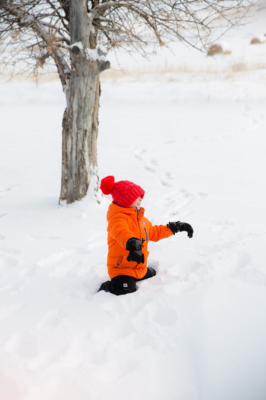 Happy child playing in deep snow wearing orange jacket