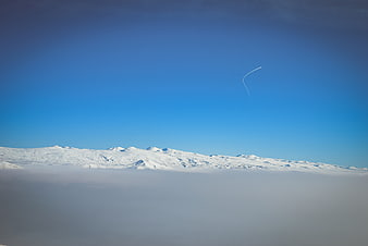 Snowy mountain peaks rising above clouds with blue sky