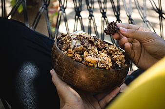 Hands holding coconut bowl of granola and nuts outdoors