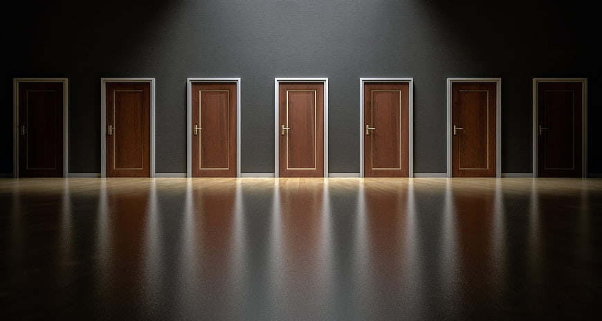 Conceptual row of wooden doors in dark hallway with spotlight