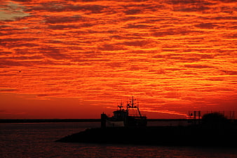 Dramatic fiery orange sunset sky over silhouetted fishing boat