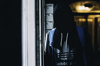 Anonymous figure in black hoodie and backpack in dark hallway