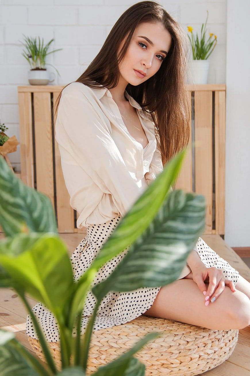 Young Woman Sitting on Woven Pouf with Plants