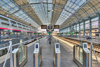 Modern train station platform with moving silver train and turnstiles