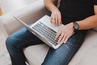 Man Typing On Silver Laptop While Sitting On Beige Sofa