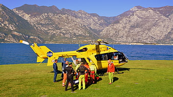 Yellow rescue helicopter on grassy field with mountains