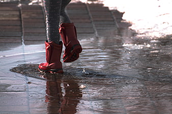 Child in red rain boots splashing in a puddle on a wet street