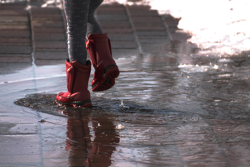 Child in red rain boots splashing in a puddle on a wet street