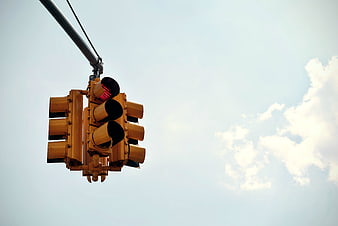 Red Traffic Light Hanging Against Blue Sky with Clouds