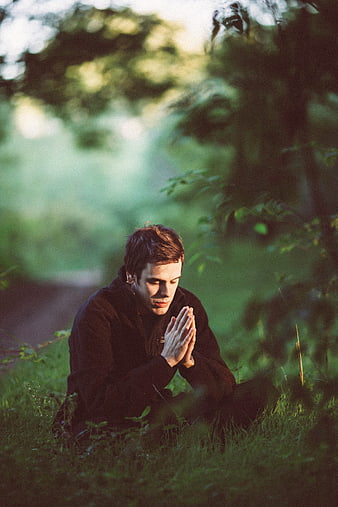 Young Man Meditating in Forest with Hands in Prayer