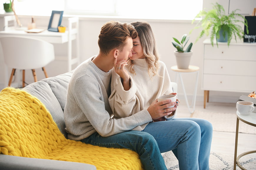 Affectionate young couple cuddling on sofa with coffee