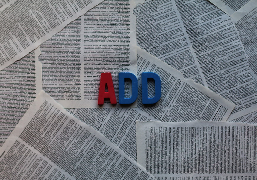 Red and blue foam letters spelling ADD on newspaper background