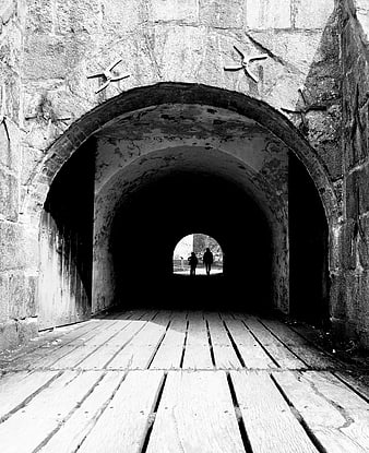 Black and white photo of stone archway tunnel with wooden floor