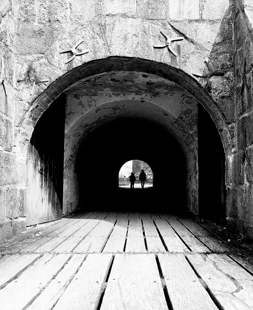 Black and white photo of stone archway tunnel with wooden floor