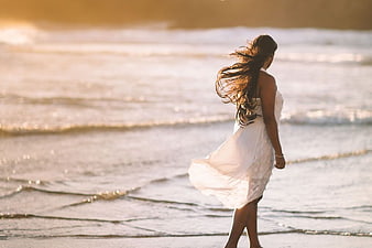 Woman in White Dress Walking on Beach at Sunset