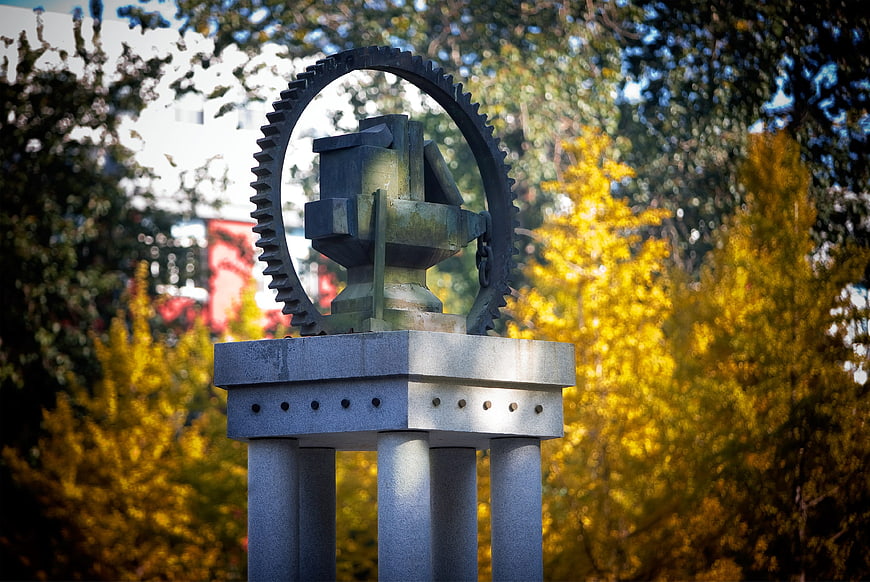 Metal Gear Sculpture on Stone Pedestal with Autumn Ginkgo Trees