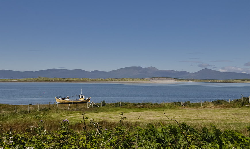 Yellow fishing boat on grassy shore with blue lake and mountains