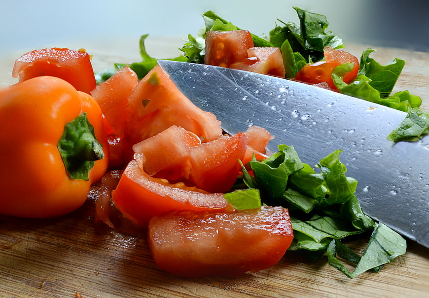Fresh chopped tomatoes, peppers, and greens on a wooden cutting board