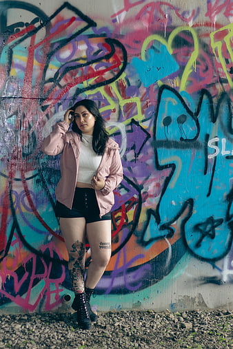 Woman with tattoos posing against colorful graffiti wall