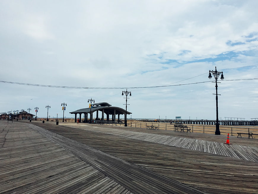 Empty wooden boardwalk with gazebo and pier under cloudy sky