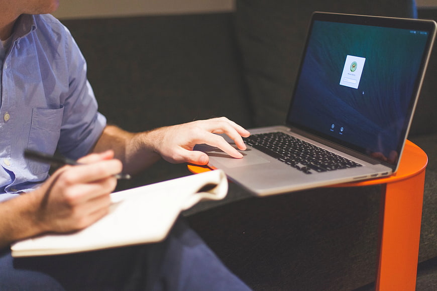 Man Writing Notes While Using Laptop