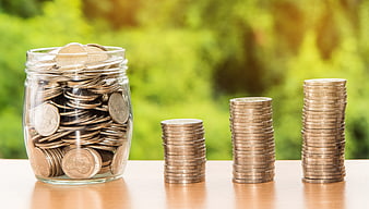 Glass jar and stacks of coins on wooden table with green background