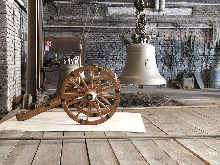 Historic wooden cannon wheel and large bell in industrial foundry