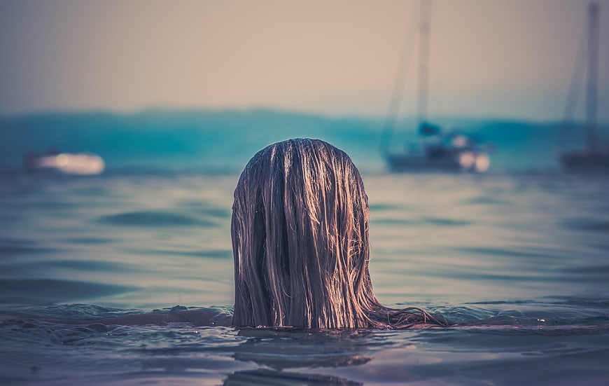 Woman swimming in ocean with wet hair and boats in background