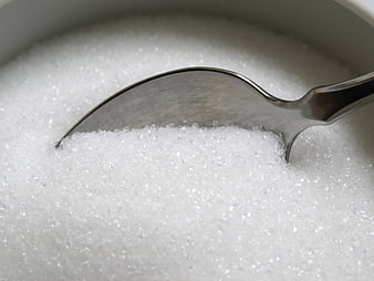 Close-up of white granulated sugar in a bowl with a metal spoon