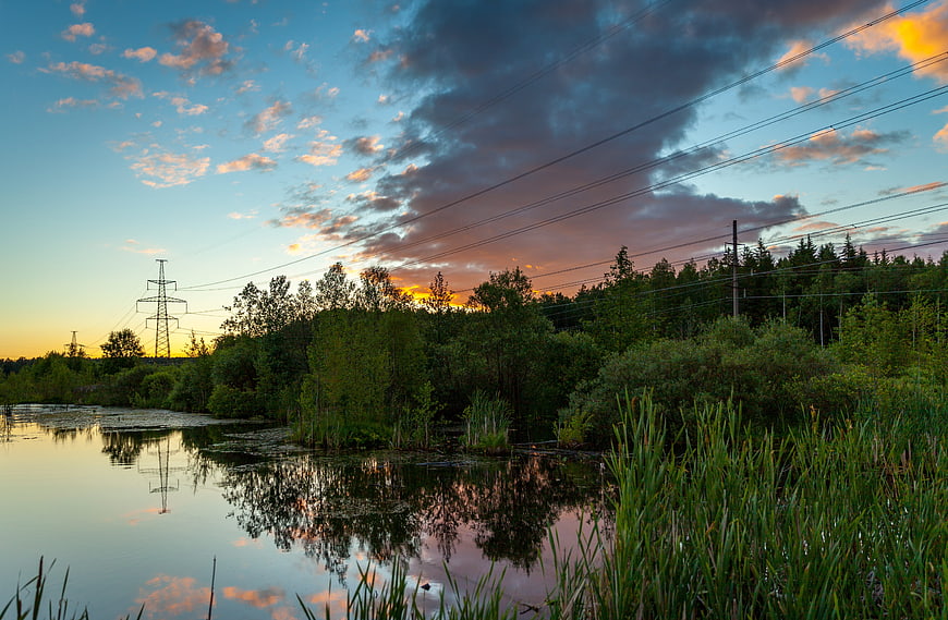 Dramatic sunset landscape with power lines and lake reflection