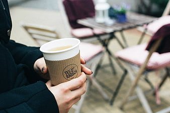 Hands holding takeaway tea cup at outdoor cafe