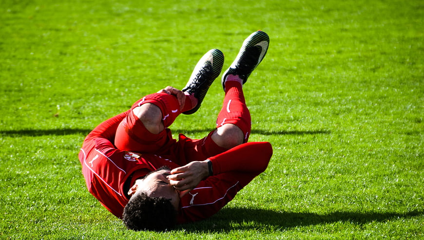 Injured soccer player clutching knee on green grass field