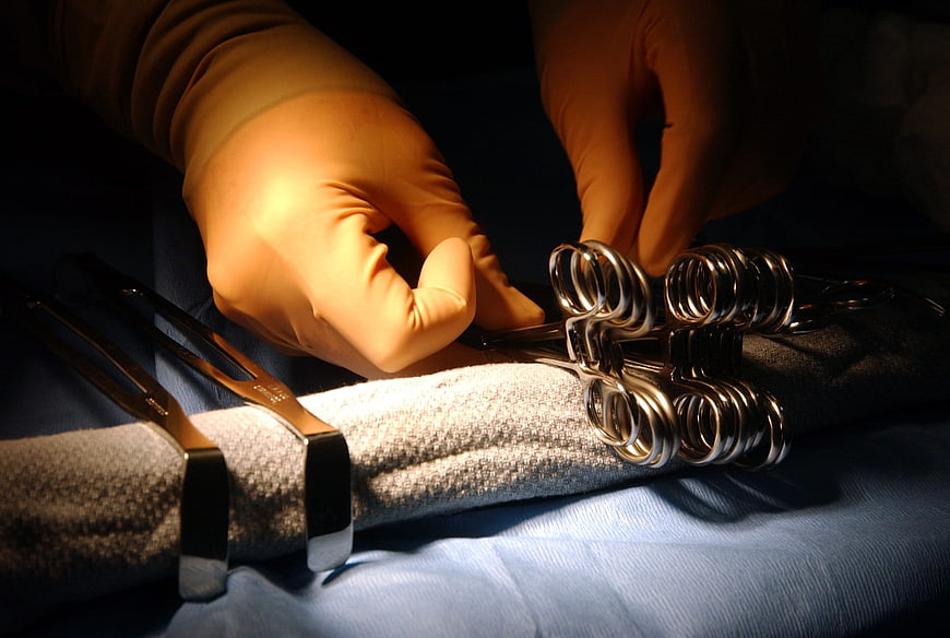 Gloved Hands Arranging Surgical Instruments on Blue Drape