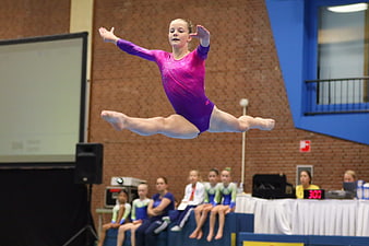 Young female gymnast performing split leap in purple leotard