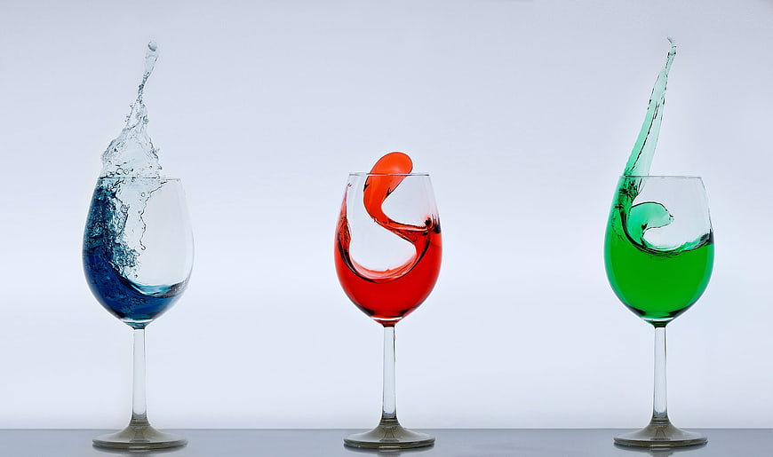 Three wine glasses with colorful liquid splashes